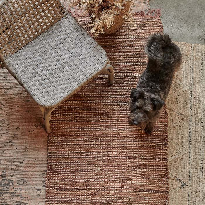 A dark fluffy dog standing on a brown woven leather runner.