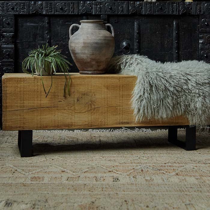 The Darby Bench, a faux wood bench with industrial looking black metal legs, with vases and a sheepskin on top.