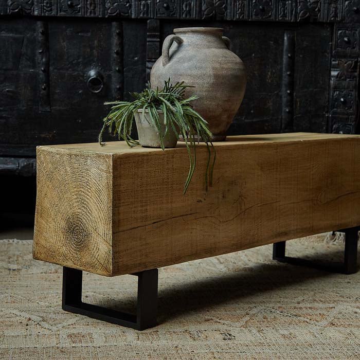 Abigail Ahern Darby Bench with a realistic wood-effect finish and industrial-style black metal legs, styled with a decorative vase and faux plant in a contemporary interior.