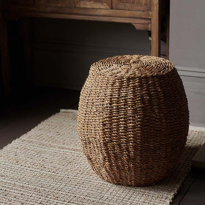The Elias Seagrass Stooll sat on the edge of a beige rug.