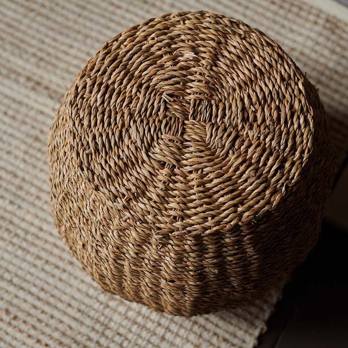 The Elias Seagrass Stool, a round stool woven in a natural brown seagrass sat on a beige rug.