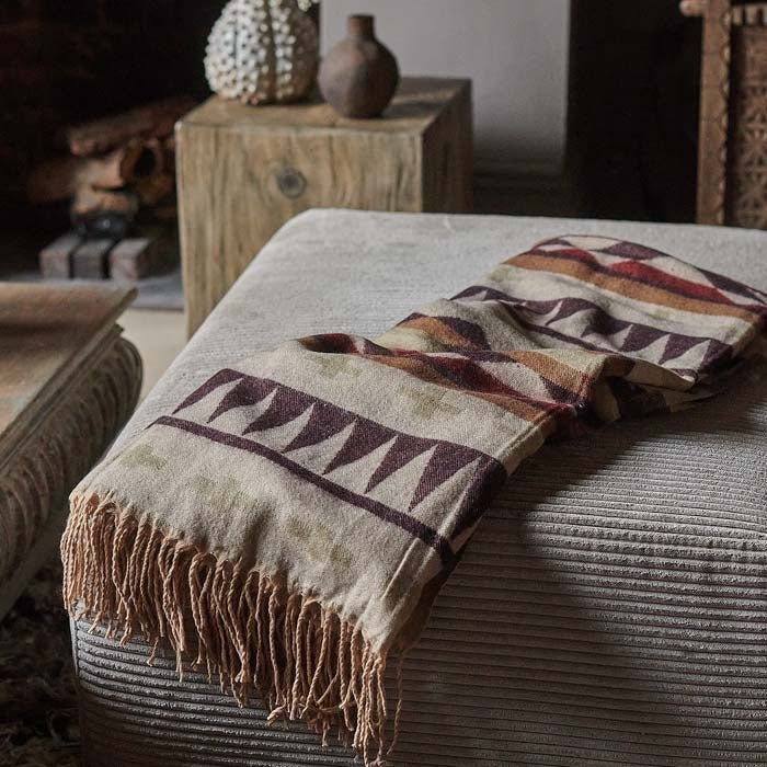 The Kensa Throw, a purple and brown patterned throw folded on a corduroy chair.
