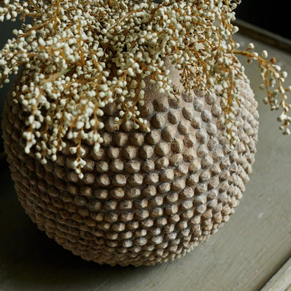 Artificial heather in a round cement vase with spiky bobble texture.