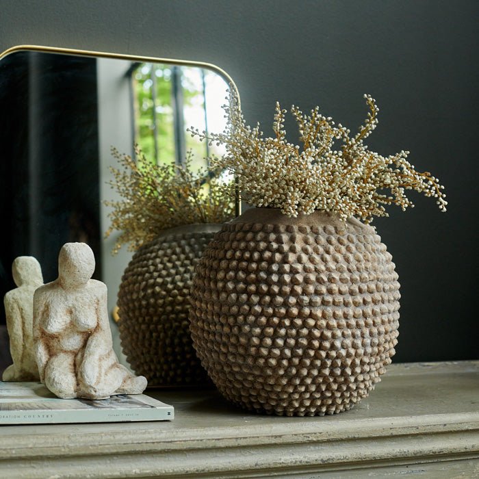 Bobbly round vase with cream flowers sat in front of a gold framed square mirror