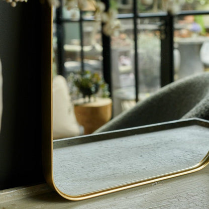 Curved edge mirror with a thin gold metal frame sat on a wooden table