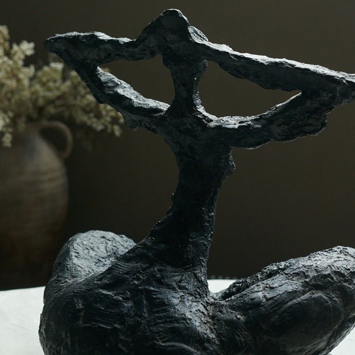 Rustic texture on black resin figurative sculpture in a female form. Large sculpture to add personality to your home styling. a cross-legged seated figure with its arms raised touching its head.