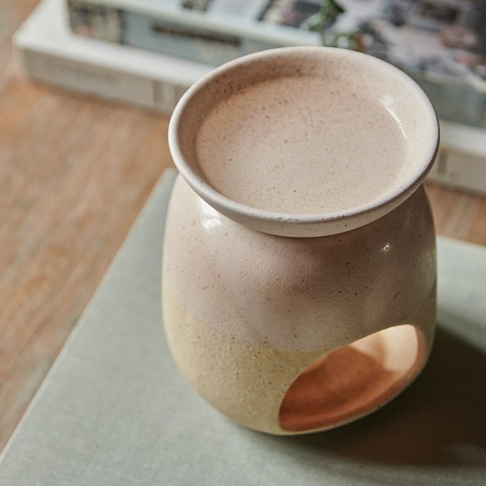 A top view of the Thea Oil Burner, a cream coloured ceramic oil burner sat on a large grey book.
