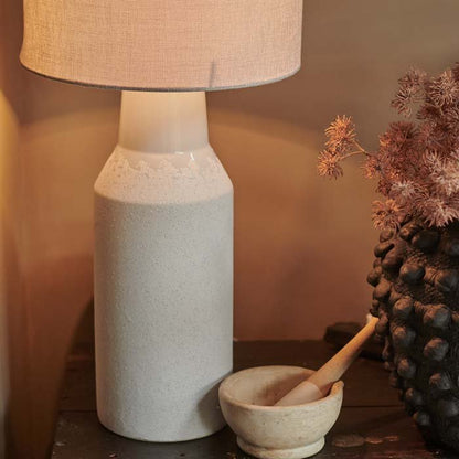 Textured cream ceramic table lamp switched on, sat on a wooden surface
