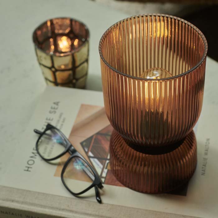 Amber hued glass LED lamp switched on, on top of a magazine