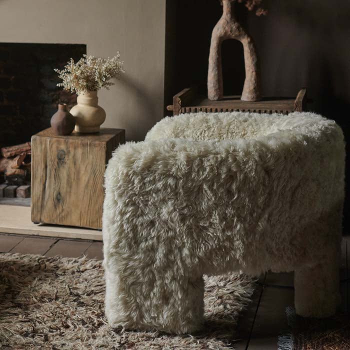 Cream sheepskin side of a three legged armchair sat in front of a fireplace
