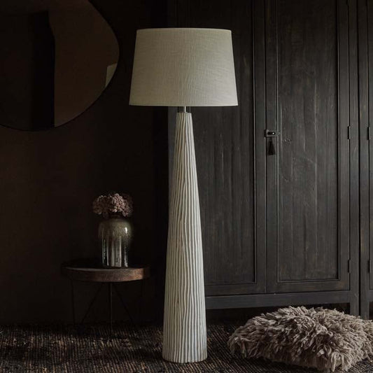 Tall textured white floor lamp with a linen lampshade in front of a wooden wardrobe