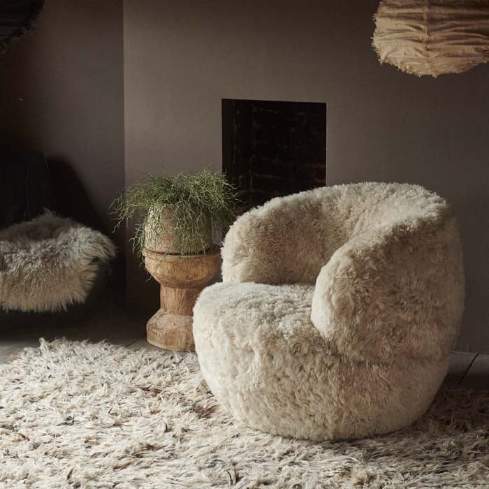 Round cream sheepskin armchair sat on a shaggy rug in front of a fireplace