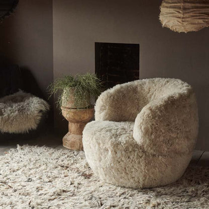 Round cream sheepskin armchair sat on a shaggy rug in front of a fireplace