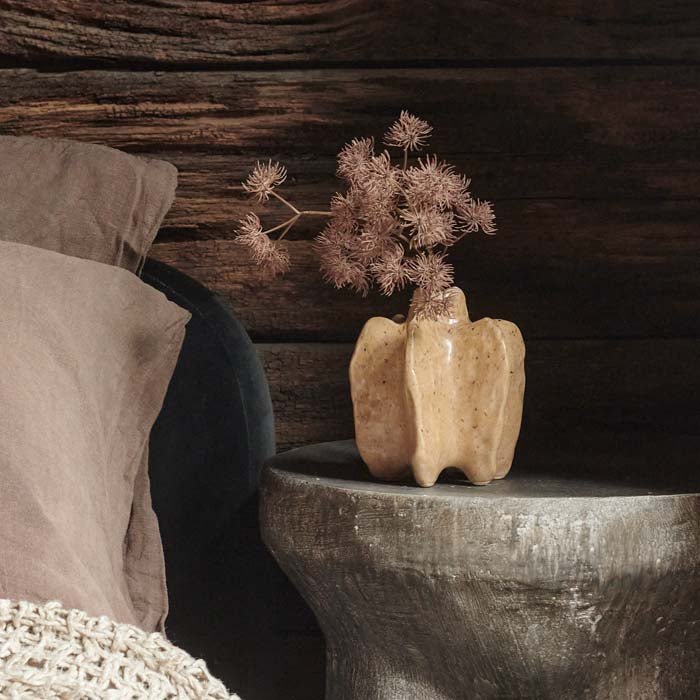 Light orange bud vase with a single textural foliage stem placed bedside
