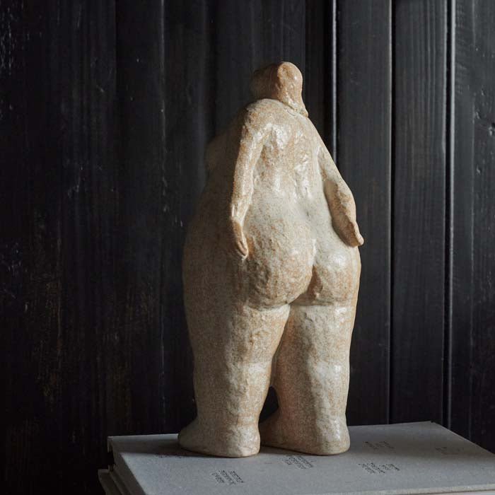 The back of a standing female sculpture styled on a stack of design books. Rear view of a curvaceous female sculpture standing with her hands behind her back.
