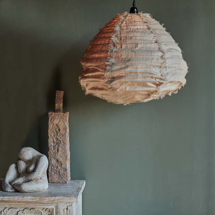Amna pear shaped fabric ceiling pendant, styled with a tall bottle vase and a sculpture. An unusual shaped pendant light in light coloured fabric. 