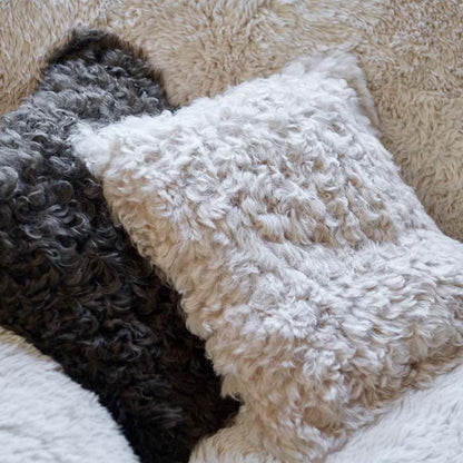 Close up image of the details on a cream, fur square cushion next to a black fur cushion