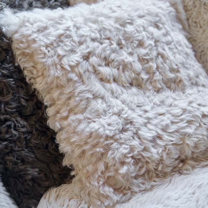 Close up image of the texture of a shaggy cream sheepskin cushion