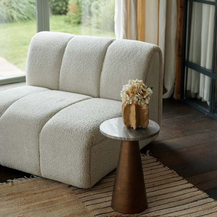 A large, armless cream occasional chair next to a side table with a faux bouquet in a vase.