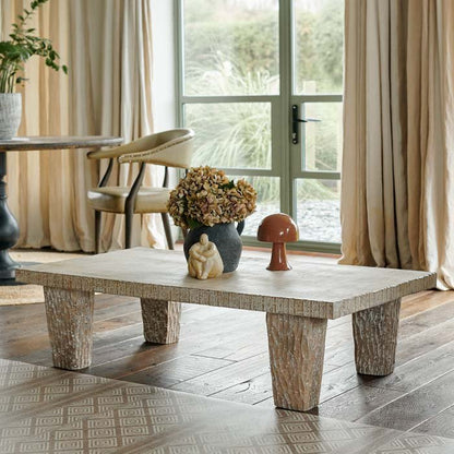 A four legged pale wooden coffee table with a lime wash finish and carved design on the legs and edge of the table.