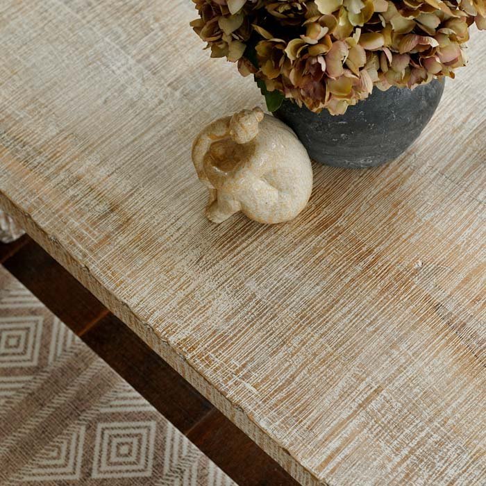 Detail image of the texture on a lime wash wood coffee table, styled with a small ceramic sculpture and a faux bouquet of flowers
