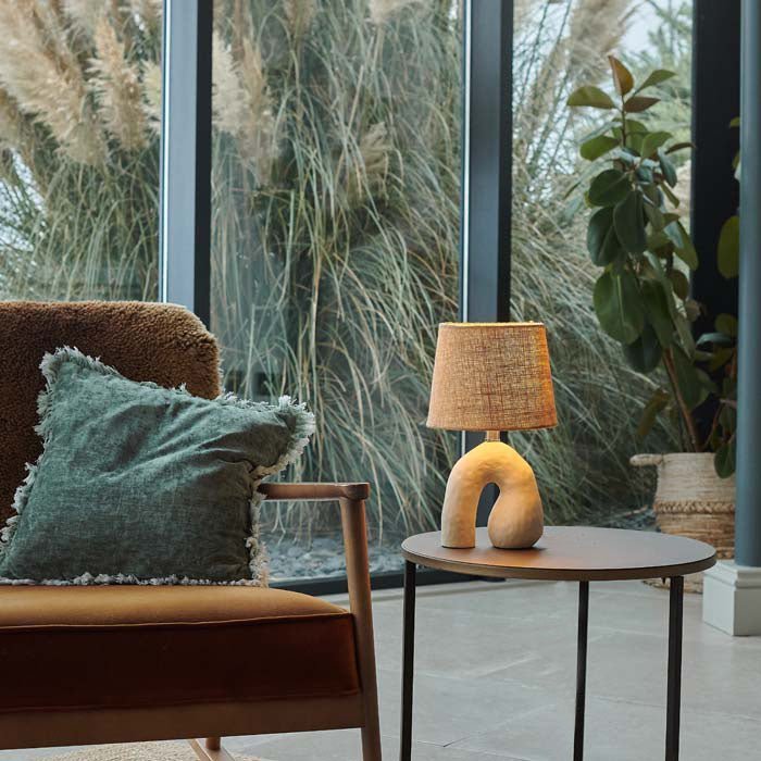 Style image of a cream, sculptural table lamp on a side table giving off a soft glow.