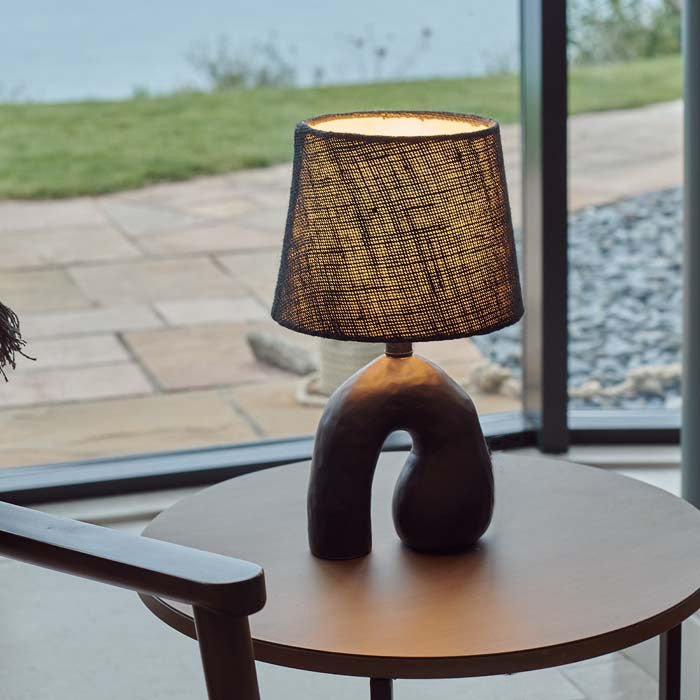 Style image of a black, sculptural table lamp on a side table giving off a soft glow.