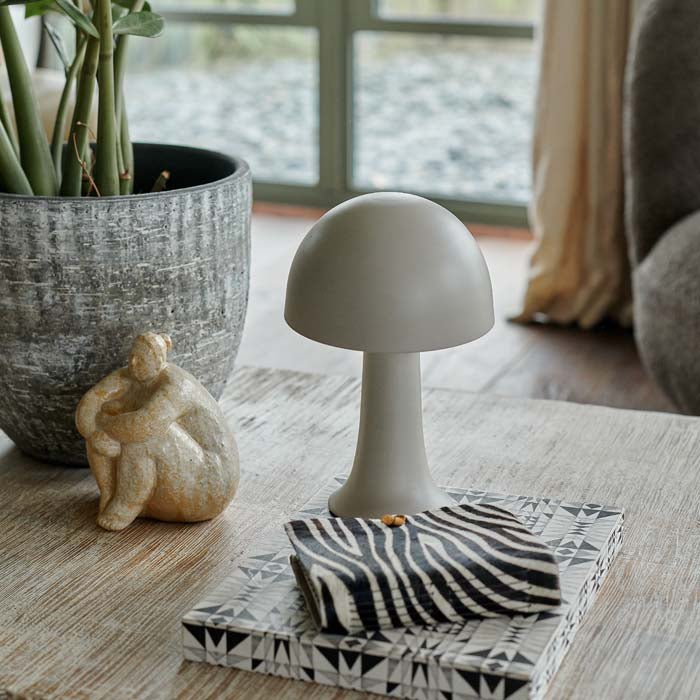 A small metal curvaceaous mushroom shaped lamp in a light neutral colour by Abigail Ahern, known for her rule breaking designs and stylish interiors. Styled on a coffee table with some books, a houseplant, these small but mighty curvy lamps are super flexible to pop all over the house, style next to your bath, bedside or create intrigue to your tablescapes and an unexpected dash of colour to your kitchen worktops.