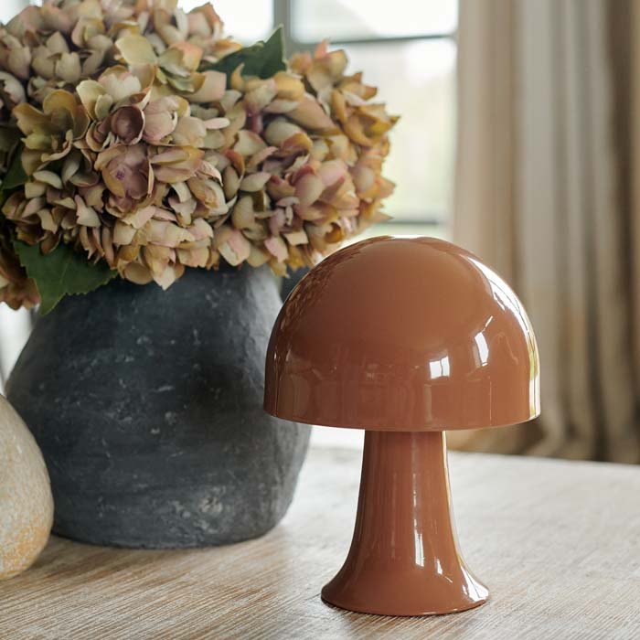 Julio LED Lamp by Abigail Ahern, known for her rule breaking designs and stylish interiors. A close up of a small portable LED table lamp in colourway called sepia which is a soft brown terracotta hue. Perfect styled on a coffee table with a vase of faux hydrangea flowers as in this vignette along with other home accessories, the perfect addition to a stylish interior. These dome shaped metal lamps are battery operated, therefore no need for plug sockets.