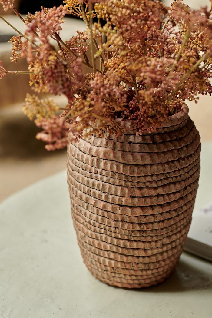 Detail images of the rustic texture of a terracotta vase with artificial flowers in it.
