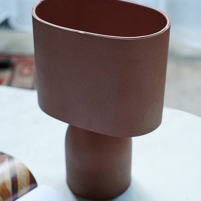 Detail image of a modern table lamp in a warm terracotta colour with a round base and matching shade.