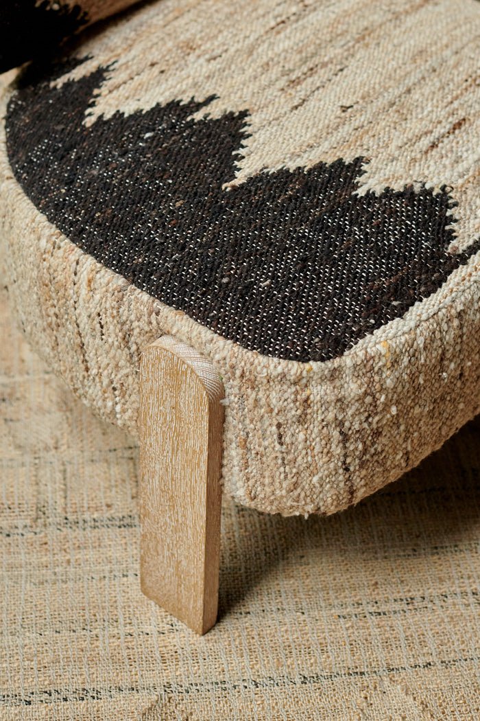 Detail of the woven wool texture of a cream chair with a black geometric pattern and wooden legs.