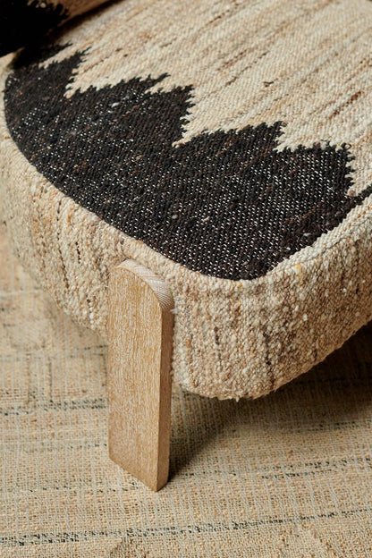 Detail of the woven wool texture of a cream chair with a black geometric pattern and wooden legs.