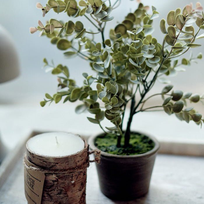 A green artificial eucalyptus plant in a pot next to a candle.