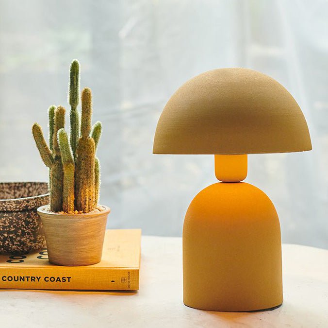 A small yellow table lamp with a round base and a matching curved, solid dome shade next to a cactus.