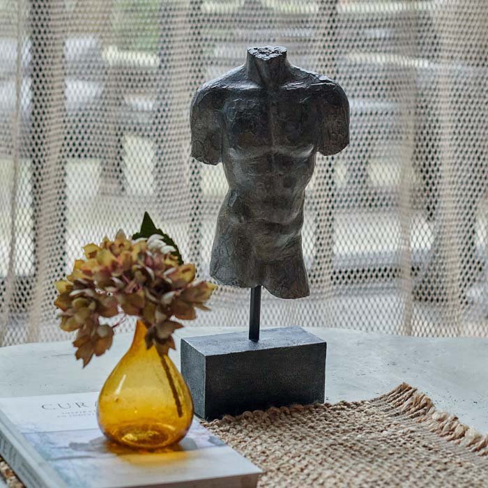 The Adonis Scultpure, a polyresin model of a male torso with a faux metal finish mounted on a small plinth, next to a vase.