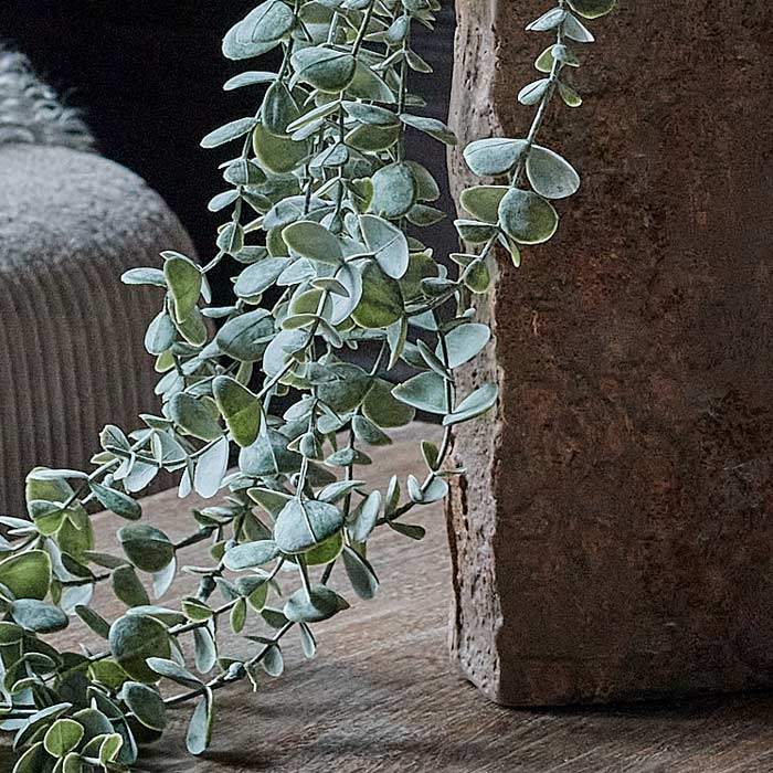 The faux trailing green eucalyptus styled in a draping way out of a brown, rough-textured ceramic vase.