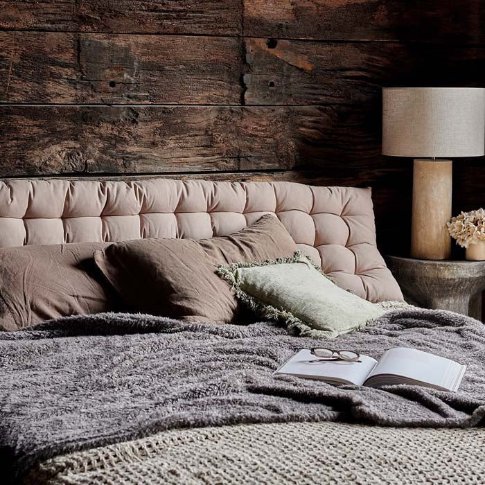 The Enrica Headboard Cushion, a sumptuous padded rectangular headboard cushion in putty coloured cotton, pictured on a cosy bed