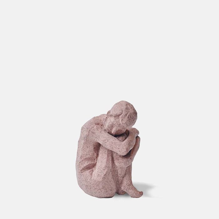 Cutout image on a white background of a small stoneware figure with its arms wrapped around its knees.