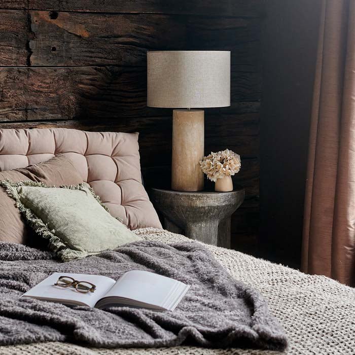 The Sennen Table Lamp, with a mottled cream coloured fibreglass base and a cream coloured drum shade on a bedside table.
