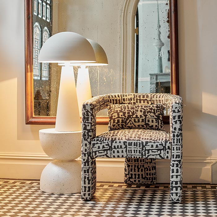 The Danby Dome Lamp, warmly lit next to a monochrome patterned chair and a large mirror.