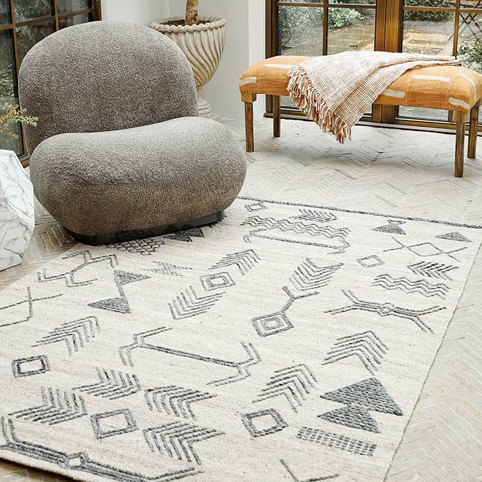 The Tampa Wool Rug, a cream rug with a beautiful black pattern in chevron style designs with a grey boucle chair.