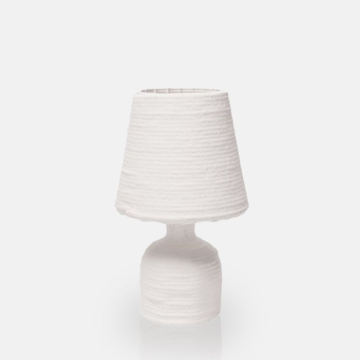 Cutout image on a white background of a small white table lamp made from paper mache with a ribbed texture.