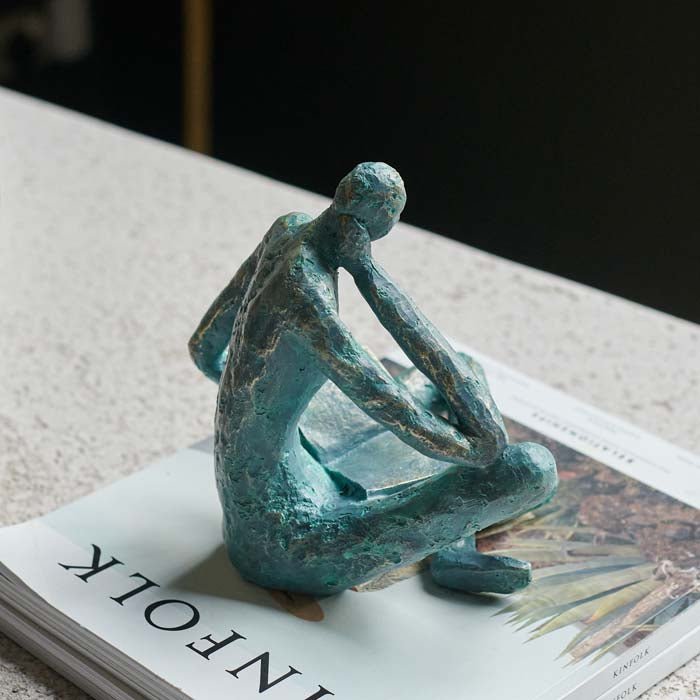 The Rollo Figurative Sculpture, a faux brass polyresin sculpture in a blue tone of a seated figure reading a book.