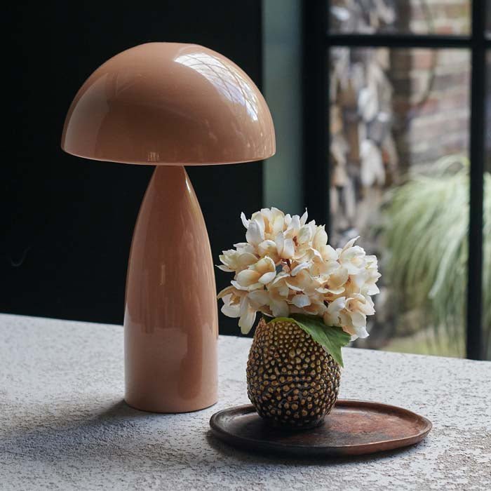 A small brown vase with a raised pebble texture holding some artificial flowers next to a pink lamp.