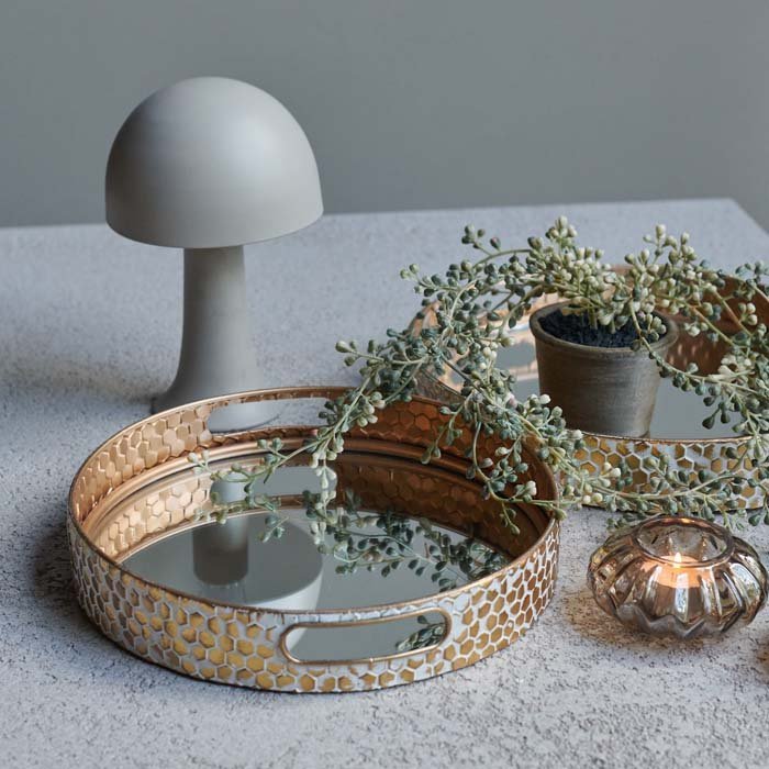 The Vola Mirrored Tray Pair, a set of two mirrored trays with gold and white honeycomb effect sides, next to a white lamp.