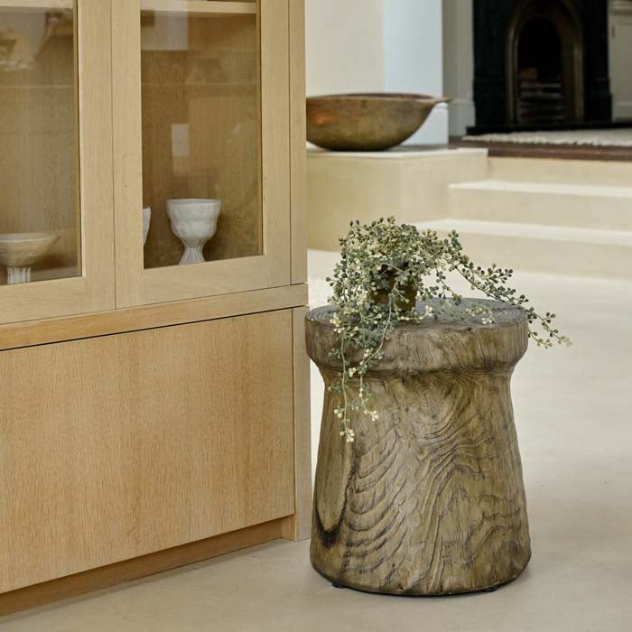 Dervio Wooden Stool, a wood-effect eco-friendly stool in a contemporary cork shape styled with a trailing potted plant.