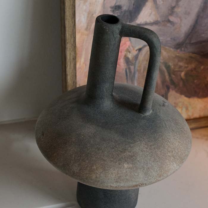 A close up of the Lovina Vase, a modernist sculptural terracotta vase with a narrow neck in a dark grey matte rustic finish.