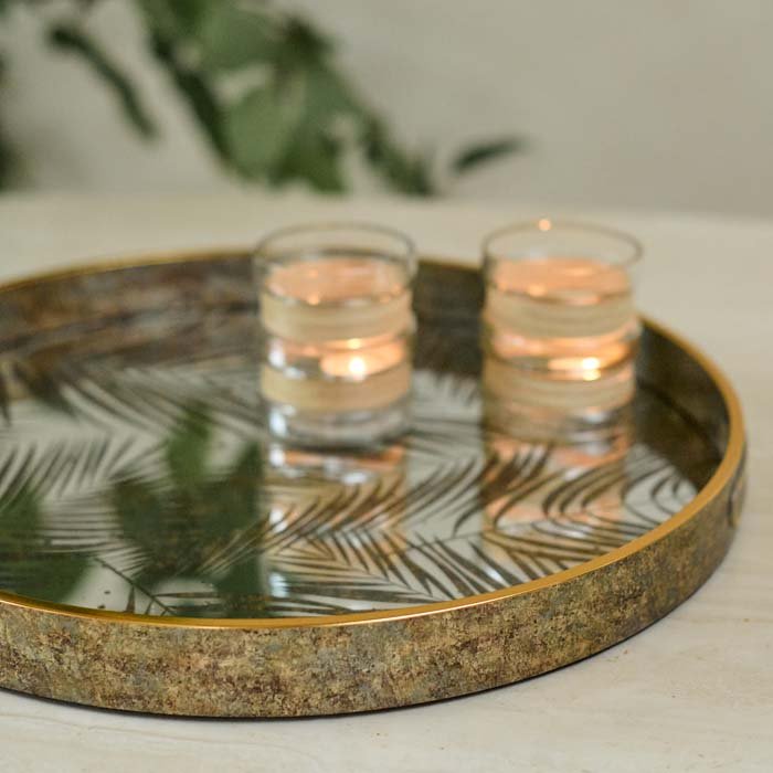 The Nassua Tray, a round tray with a mirrored surface featuring a botanical design, with a pair of glass votives.