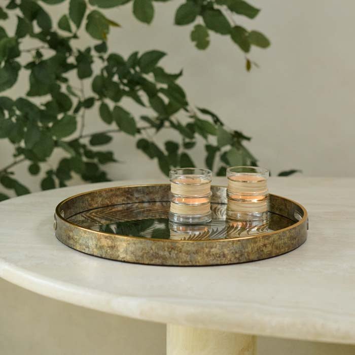 The Nassua Tray, a round tray with a mirrored surface featuring a botanical design, with a pair of glass votives.